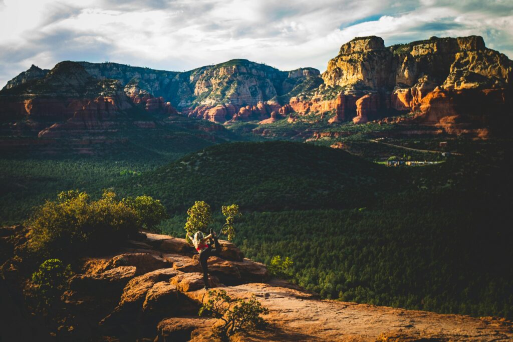 Woman performing yoga pose on a rocky ledge against the stunning Sedona landscape during sunset.
