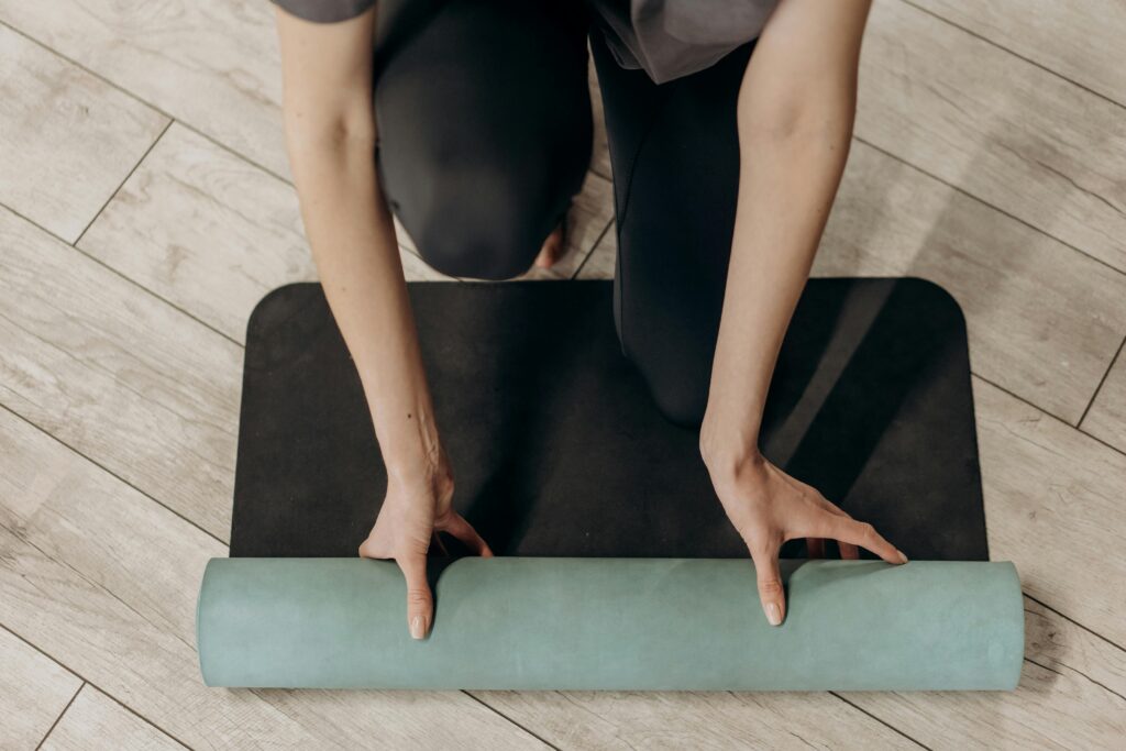 Close-up of individual rolling out a yoga mat on wooden floor, ready for a home workout.